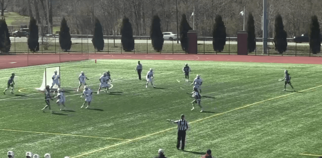 A lacrosse player wearing a white and light blue jersey prepares to throw the ball mid-stride during a game.